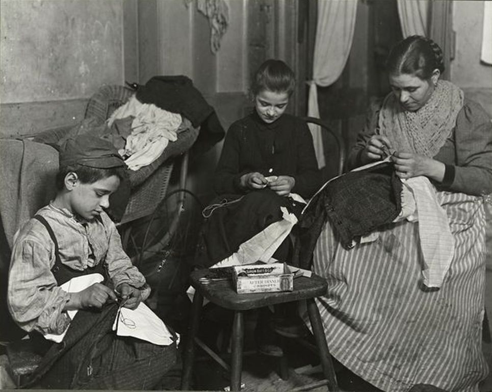 Г-жа Батталья, Тесси, 12 лет и Тони, 7 заканчивают пошив мужских брюк, январь 1908